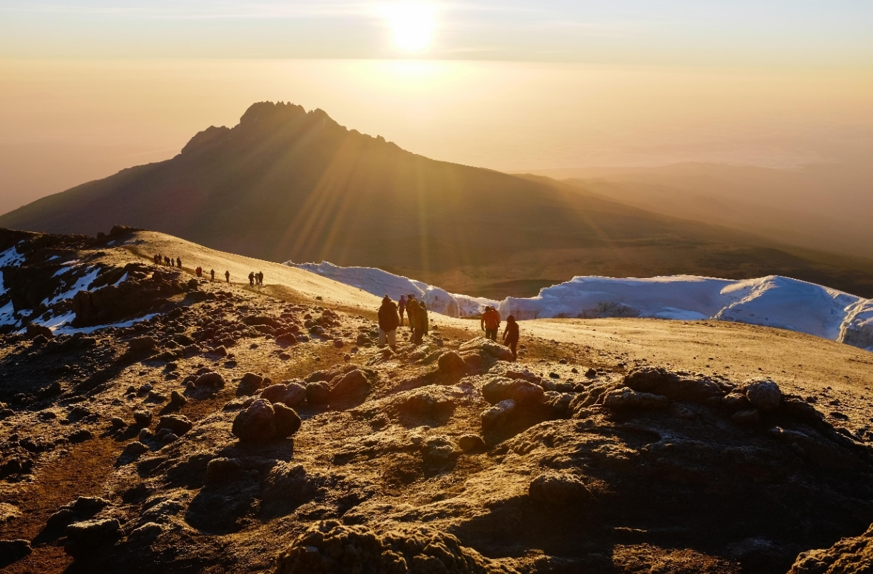 Climbers descending Kilimanjaro at sunrise above snow and volcanic ridges