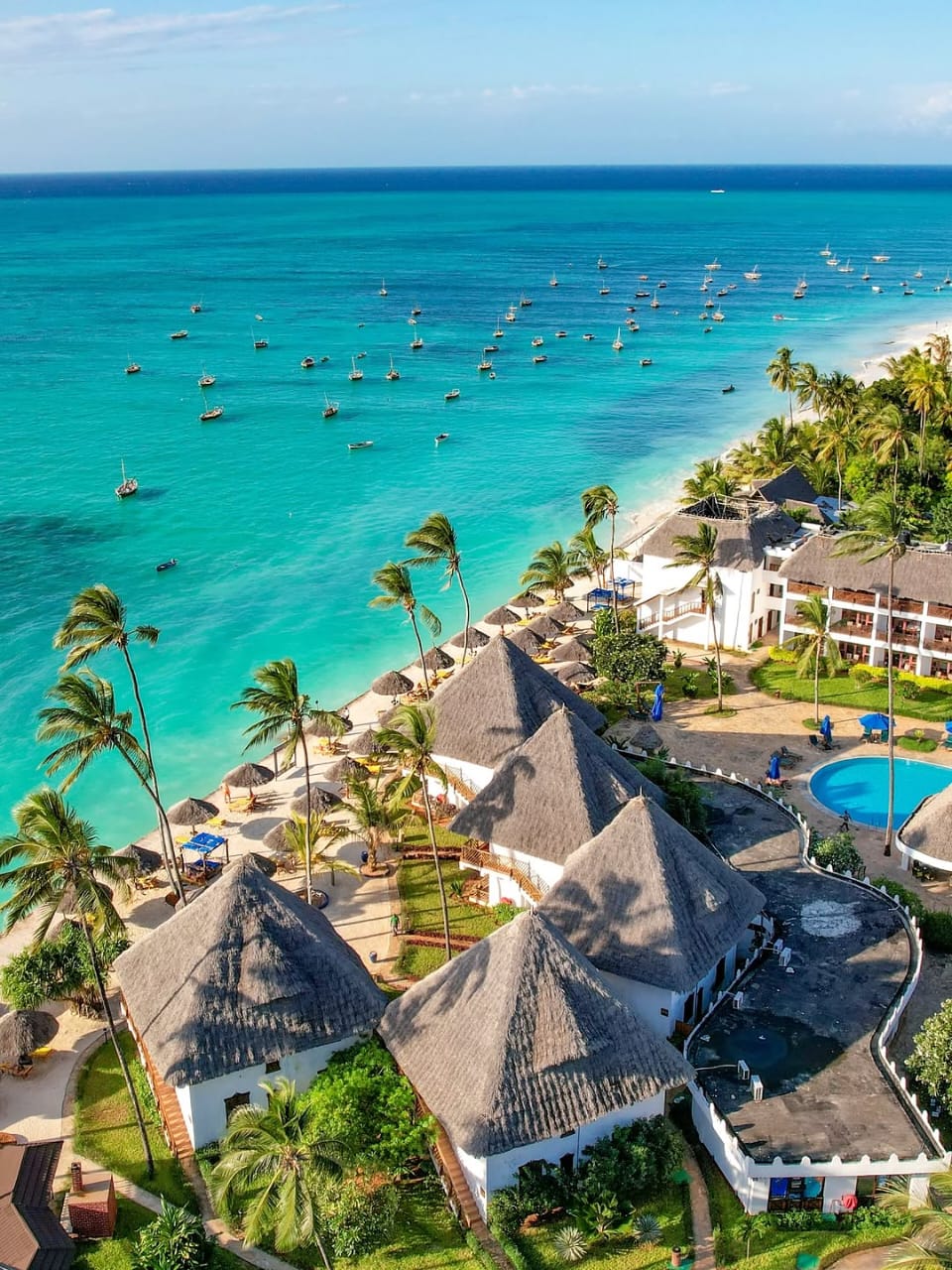 Aerial view of a palm-lined Zanzibar beach resort beside turquoise water and anchored boats